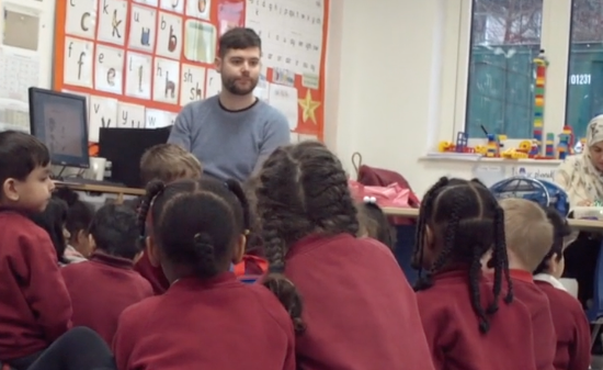 A group of primary school children sat on the floor listening to the teacher.