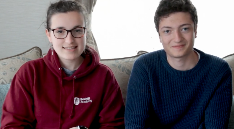 A brother and sister smiling, sitting together on a sofa.