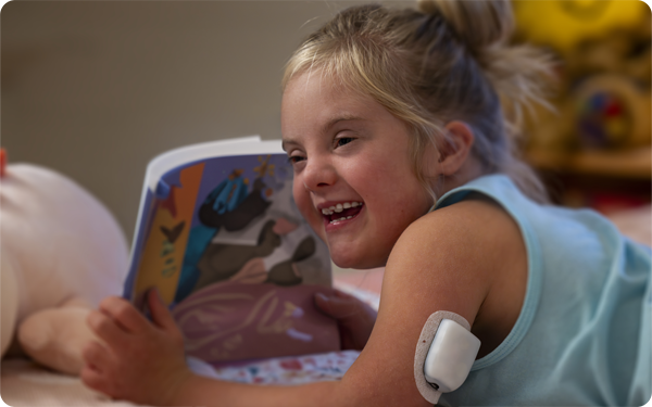 A young girl wearing an omnipod whilst reading a book.