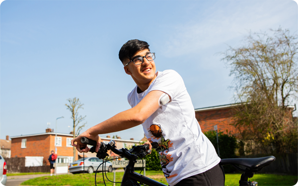 A teenage boy stands with his bike, looking behind him. He is wearing an omnipod.