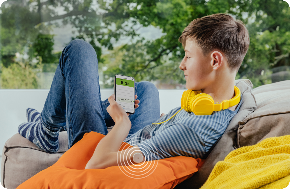 A boy sat on a chair outside looking at his glucose levels on his phone.
