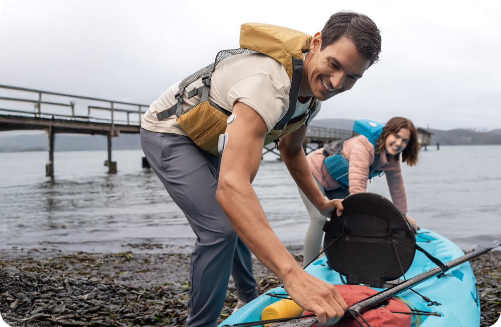A man and a woman are preparing a canoe to go into a lake. There is a pier behind them.