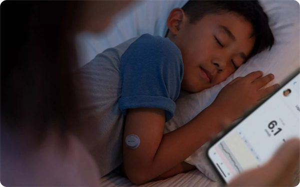 A young boy is asleep in bed whilst his mum checks his glucose levels on her phone.