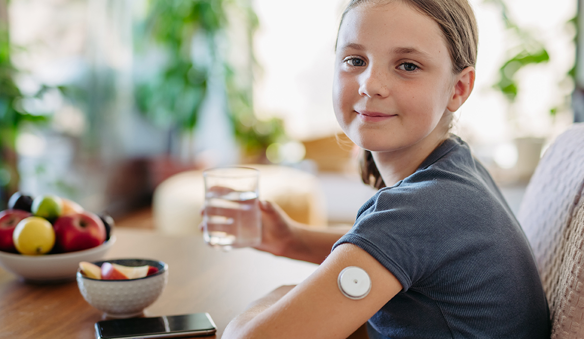 A young girl looks at the camera and smiles whilst wearing a CGM