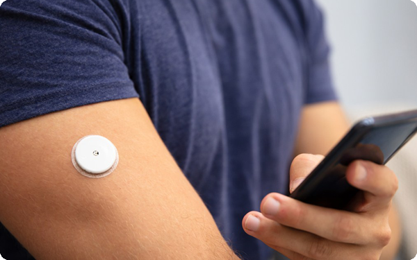 A man holding a phone with a glucose monitor on his arm.