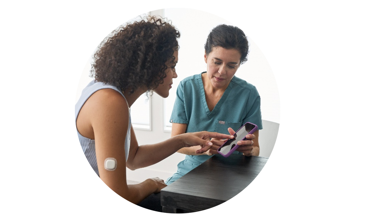 A nurse sits and shows a woman an online training platform on her phone.