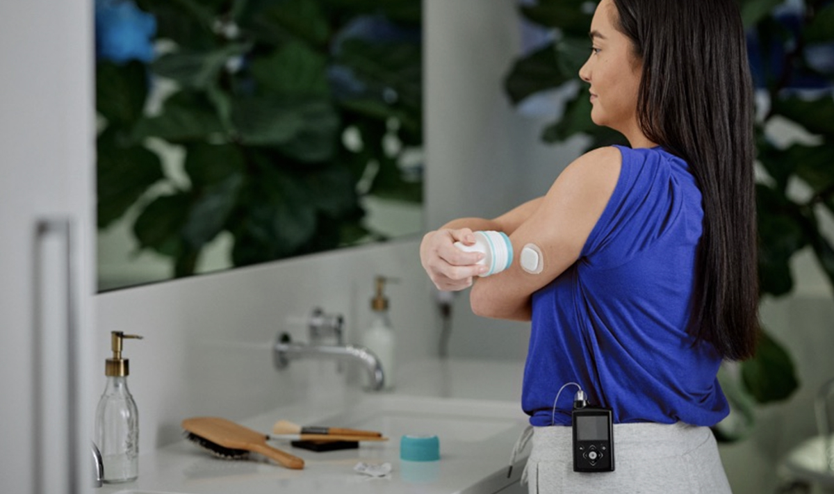 A woman is stood looking in the mirror as she applies her cgm.