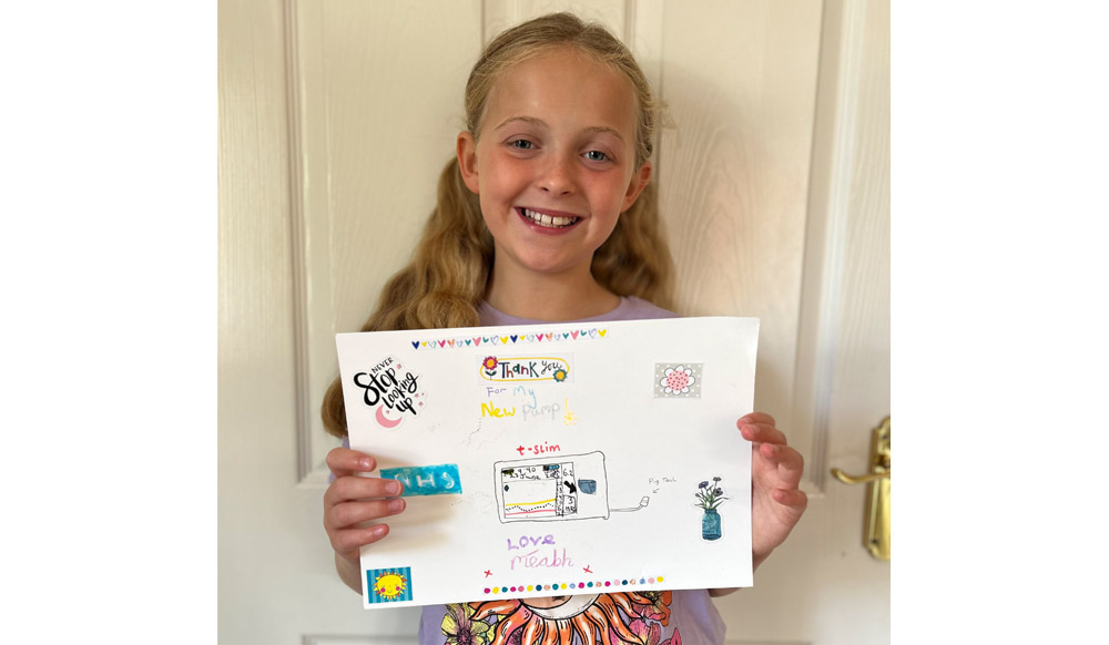 A girl stands smiling holding a picture she has drawn.